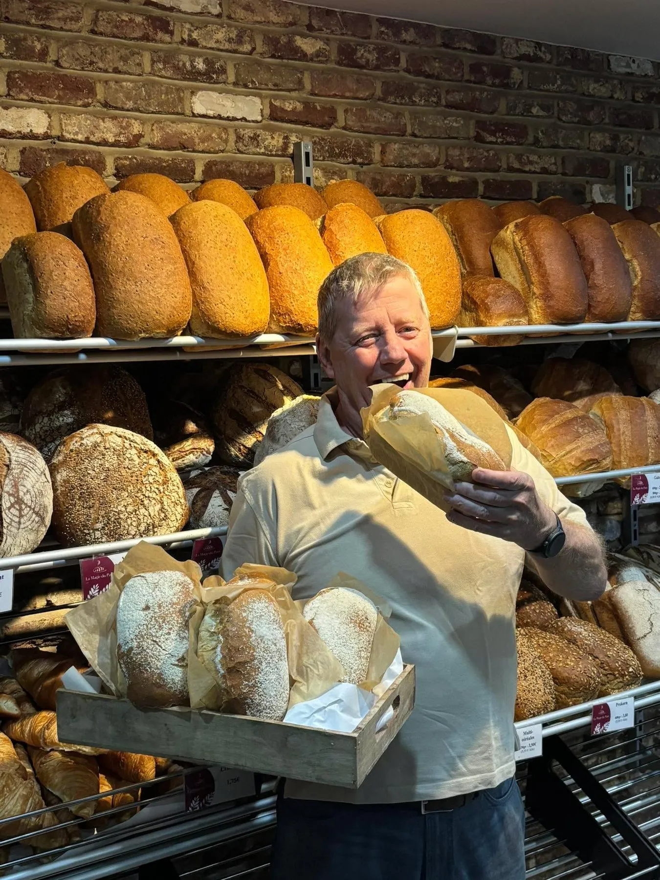 Alain, tout sourire, avec une brassée de pains devant les étagères